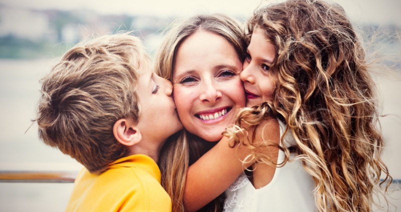 a happy mother with her young son and daughter smiling thinking about early orthodontic treatment